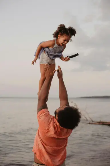 A man lifting young daughter on beach, benefitting from integrative psychiatric therapy and counseling