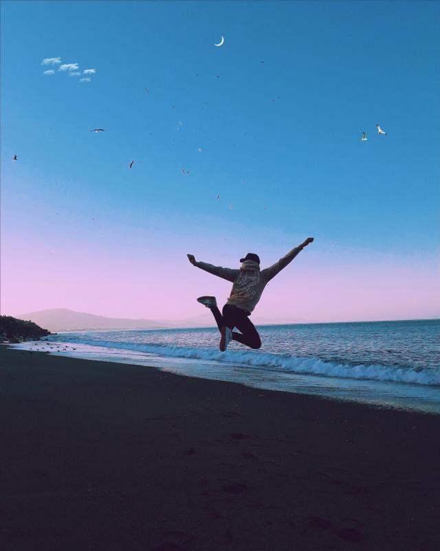 A man jumping on the beach at sunset celebrating his milestones made through life coaching in Wake Forest, NC